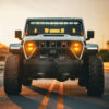 Gray Jeep Wrangler JL with jeep gladiator headlights glowing amber warm light driving on road at sunset golden hour, lifestyle installation shot