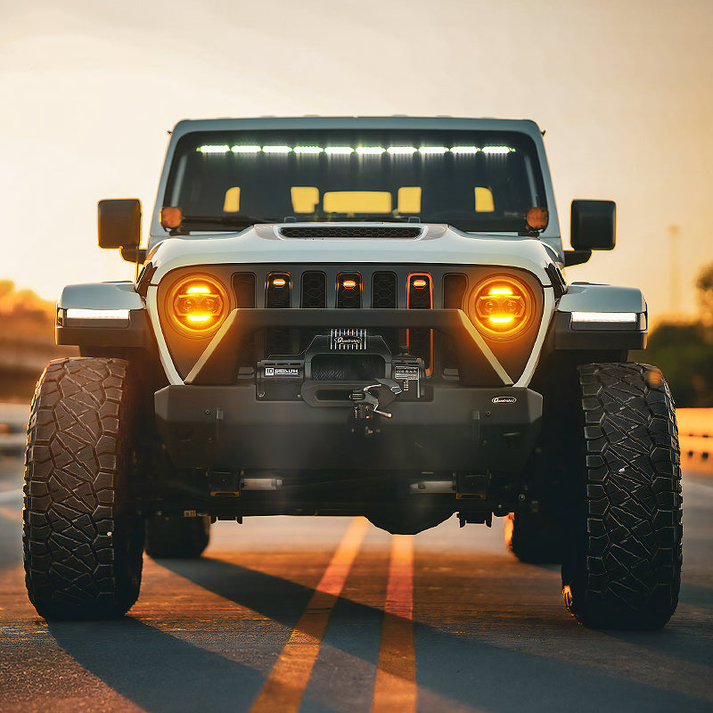 Gray Jeep Wrangler JL with jeep gladiator headlights glowing amber warm light driving on road at sunset golden hour, lifestyle installation shot