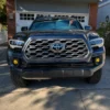 Front view of a dark blue third-generation Toyota Tacoma showing two four-module yellow fog lights mounted in the lower bumper