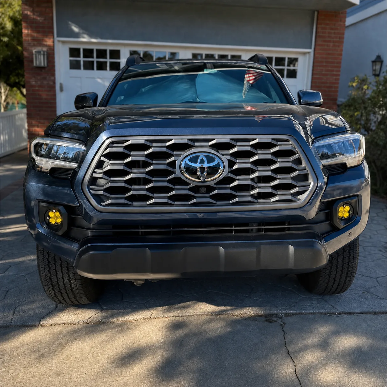Front view of a dark blue third-generation Toyota Tacoma showing two four-module yellow fog lights mounted in the lower bumper