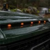 Five amber marker lights reflected on the wet hood of a dark green truck