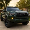 Green third-generation Toyota Tacoma on a driveway with four-module yellow LED fog lights installed in the factory bumper openings