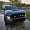 Blue Toyota Tacoma at dusk with white DRL fang lights illuminated on both sides of the front grille