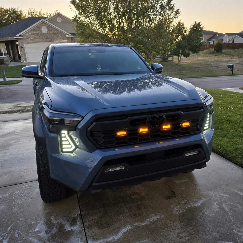Blue Toyota Tacoma at dusk with white DRL fang lights illuminated on both sides of the front grille