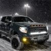 Dark Toyota Tundra parked in heavy snow with bright white headlights amber marker lights and yellow bumper fog lights