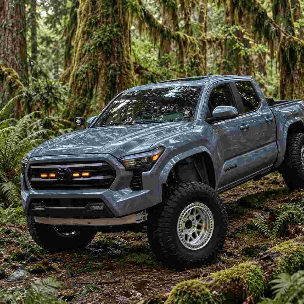 Toyota Tacoma front grill lights installed with amber illumination on an off-road truck in a forest setting